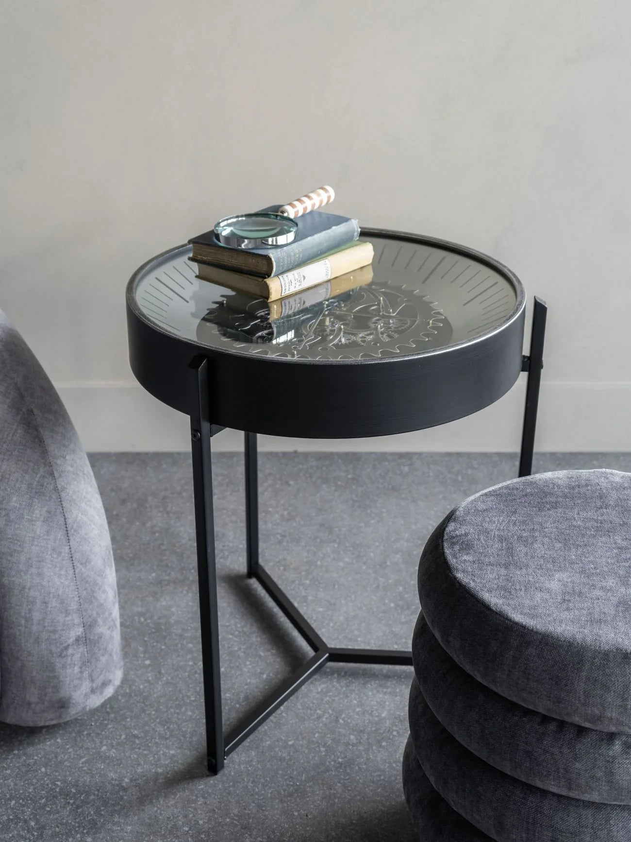 Black metal side table with glass top displaying books and a magnifying glass.