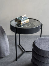 Black metal side table with glass top displaying books and a magnifying glass.