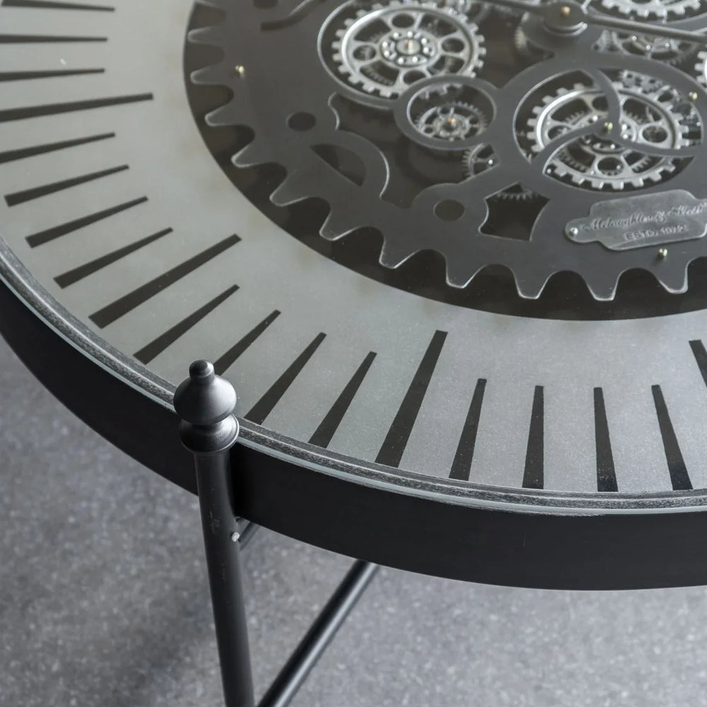 Black metal clock table with intricate moving gears and Roman numerals.