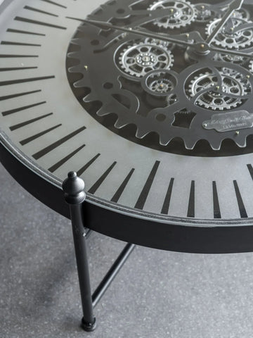 Black metal clock table with intricate moving gears and Roman numerals.