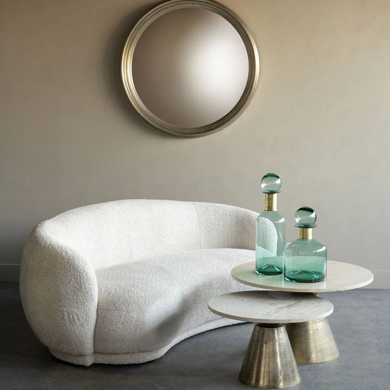 Small travertine and brass coffee table with glass vases, next to a white boucle sofa.