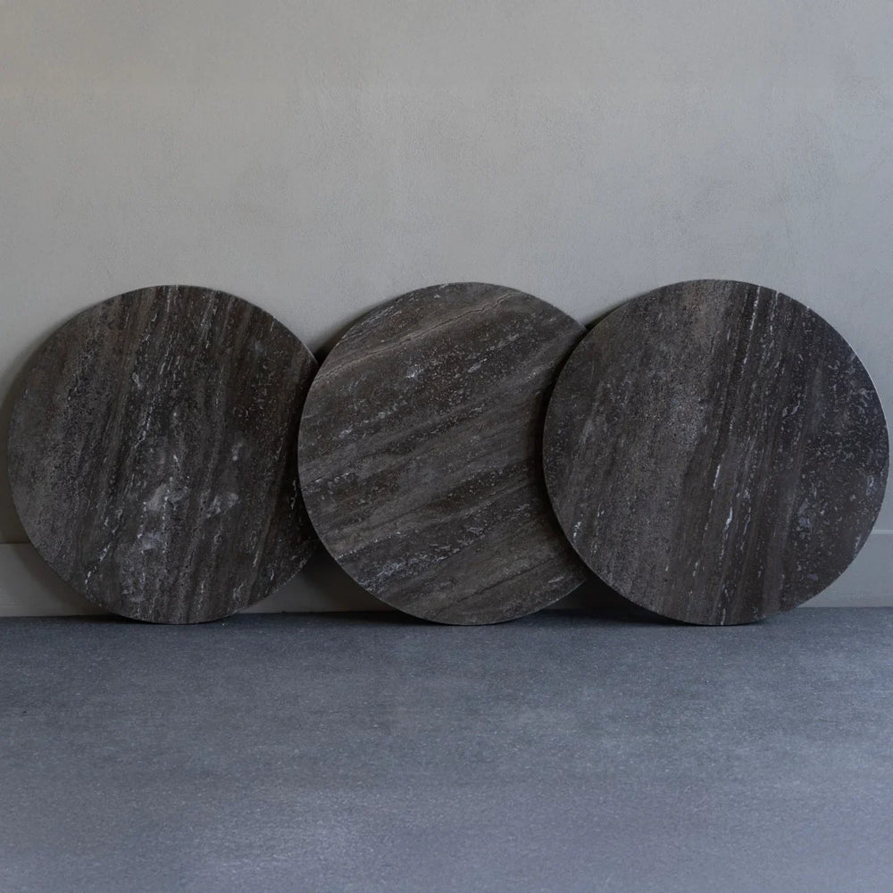 Three dark travertine round tabletops leaning against a wall.