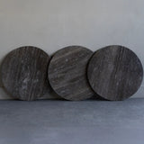 Three dark travertine round tabletops leaning against a wall.