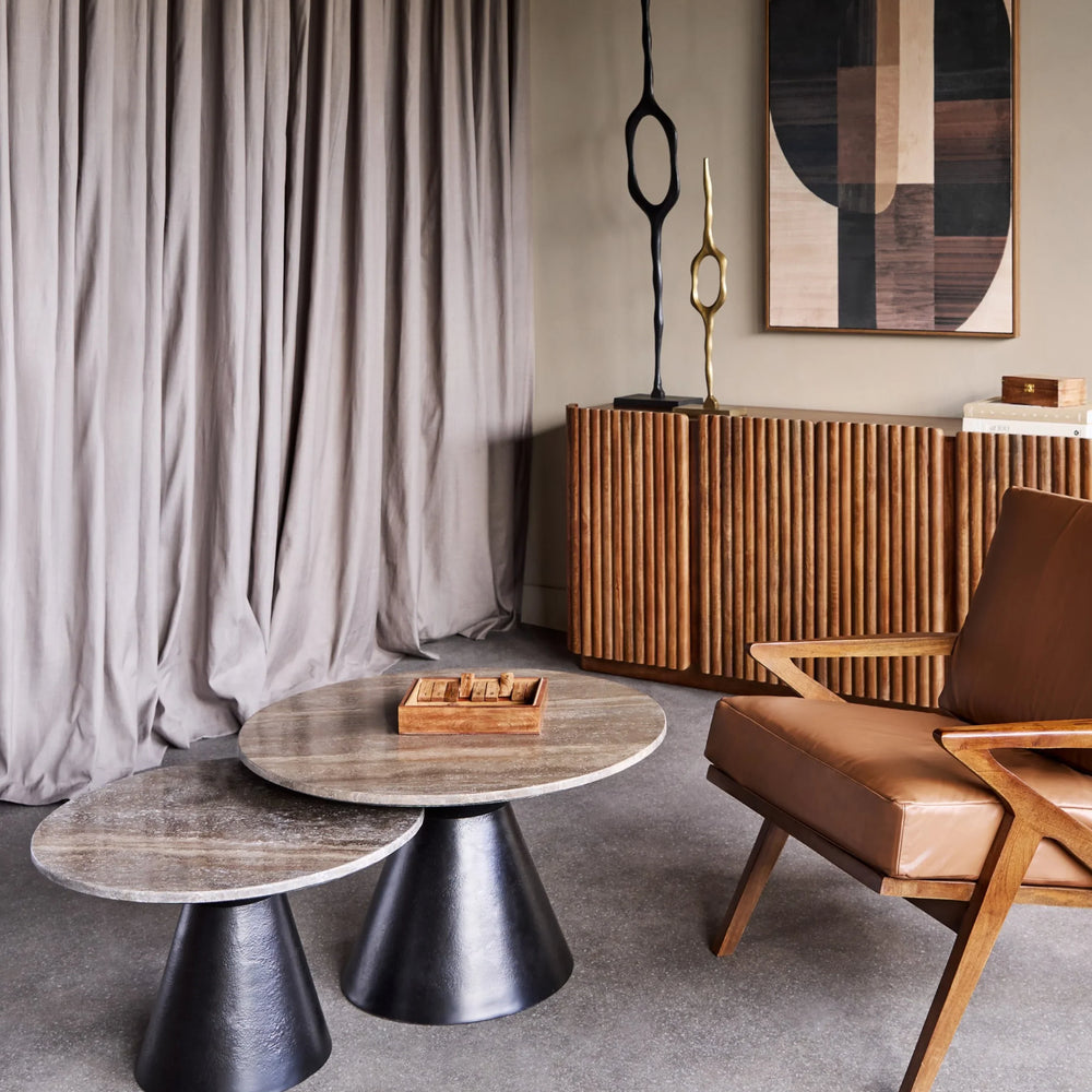 Round travertine coffee tables in modern living room with wooden chair and decor.
