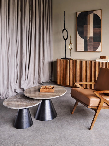 Round travertine coffee tables in modern living room with wooden chair and decor.