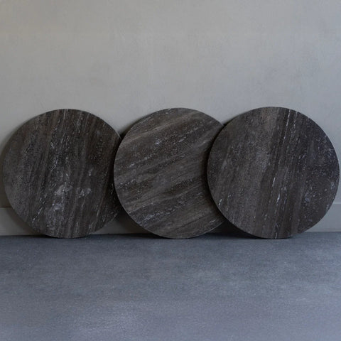 Three round dark travertine tabletops leaning against a wall.