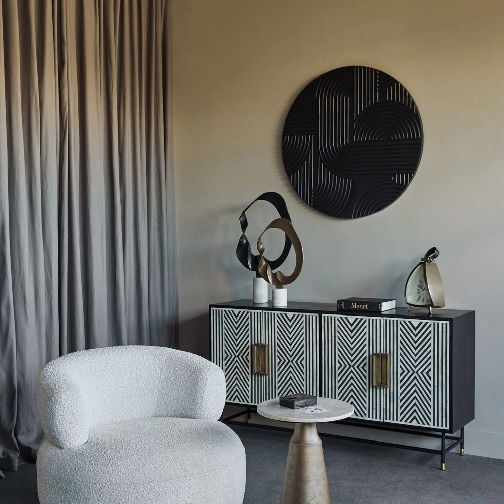 Light travertine side table in modern living room with white chair and patterned cabinet.