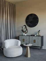 Light travertine side table in modern living room with white chair and patterned cabinet.