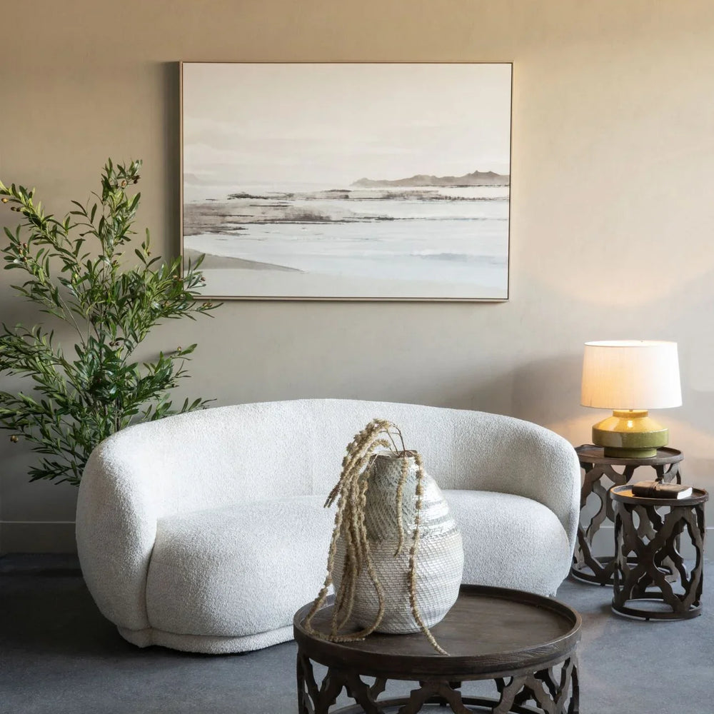 Cream curved sofa in cozy room with wooden tables and greenery.