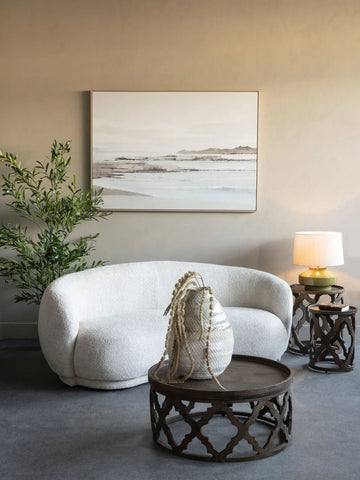 Cream curved sofa in cozy room with wooden tables and greenery.