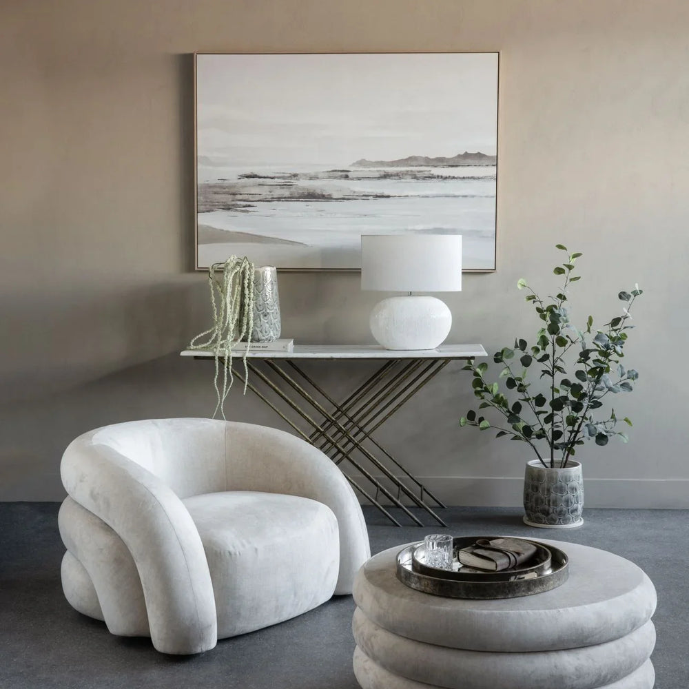 Cream ottoman and chair in elegant living room with art and plants.