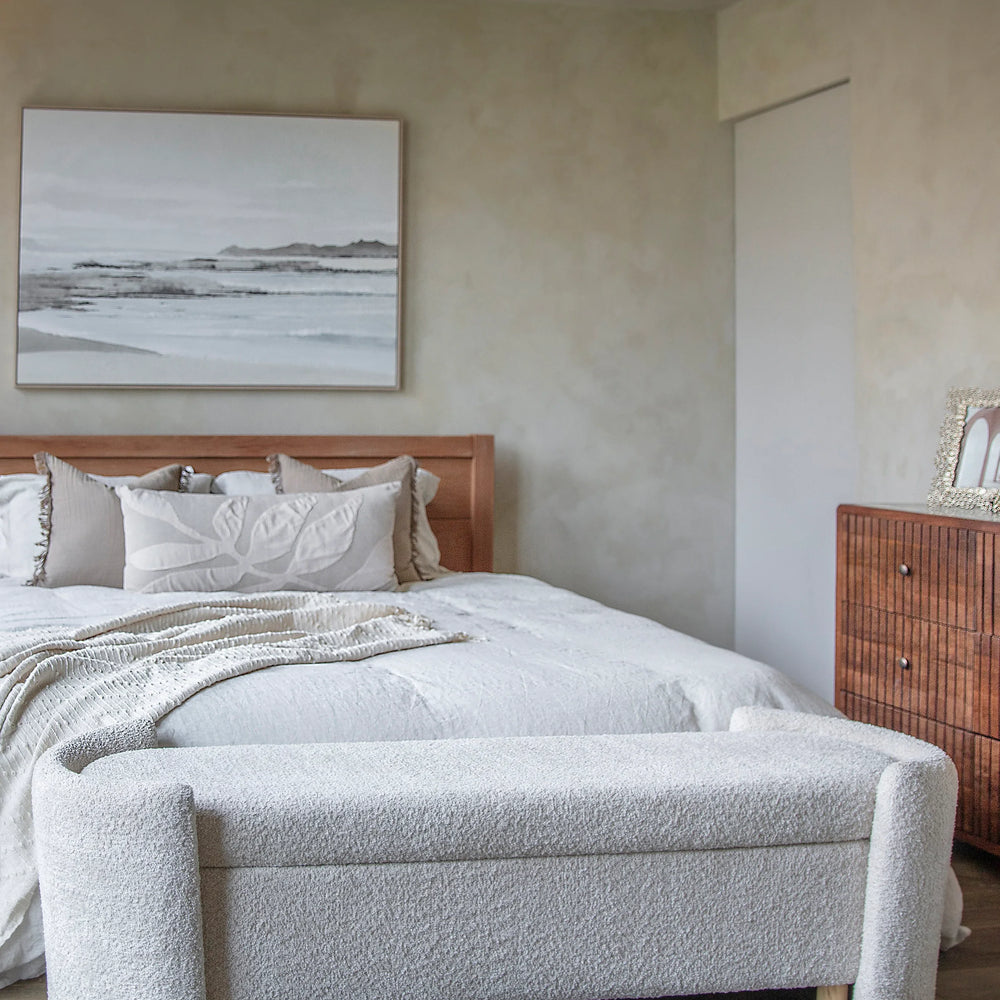 Cream upholstered bench at the foot of a bed in a cozy bedroom setting.