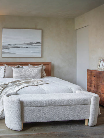 Cream upholstered bench at the foot of a bed in a cozy bedroom setting.