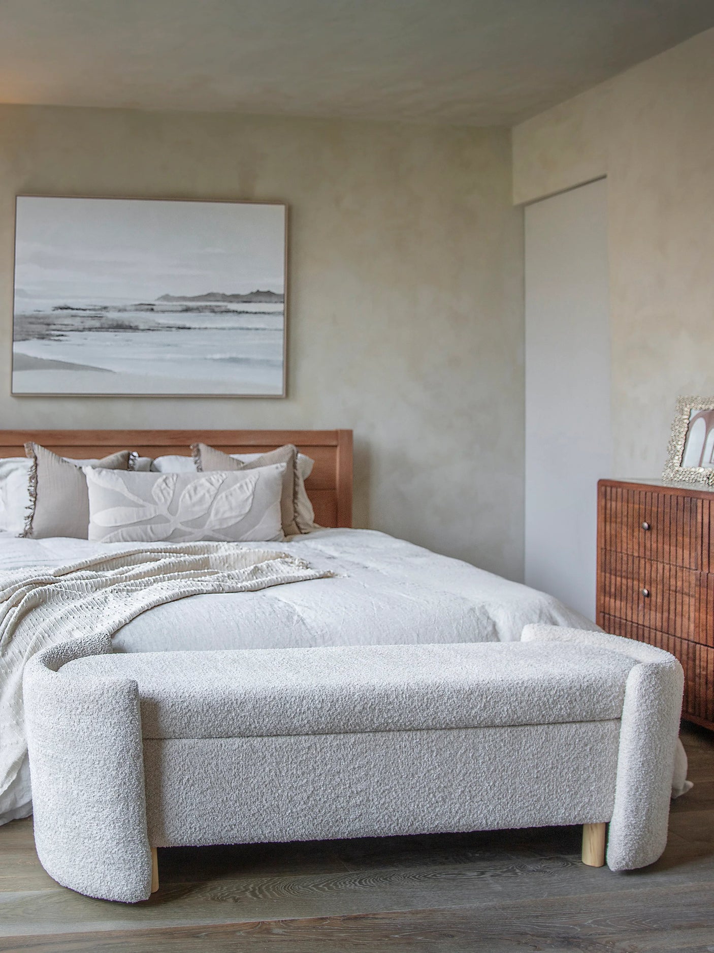 Cream upholstered bench at the foot of a bed in a cozy bedroom setting.