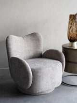 Neutral upholstered swivel chair beside a round side table with a patterned vase.