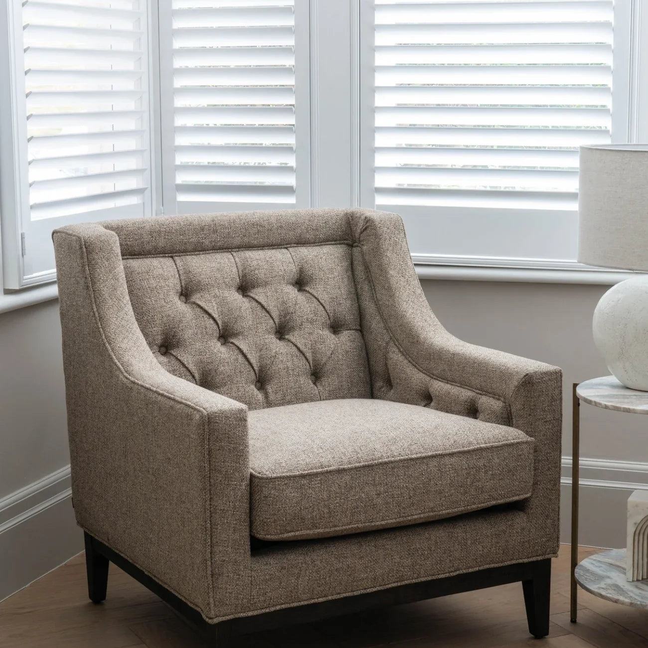 Taupe armchair with buttoned back in a bright room with shutters.