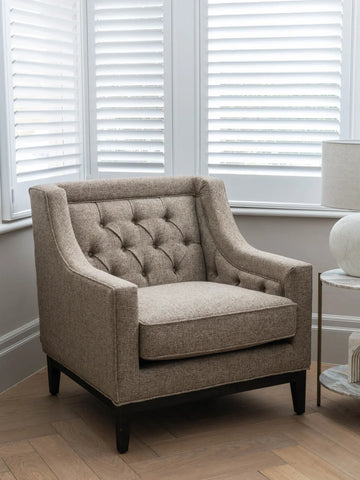 Taupe armchair with buttoned back in a bright room with shutters.