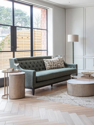 Forest green sofa in elegant living room with wooden tables and floor lamp.
