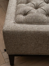 Dark taupe stool corner with buttoned texture and wooden leg detail.