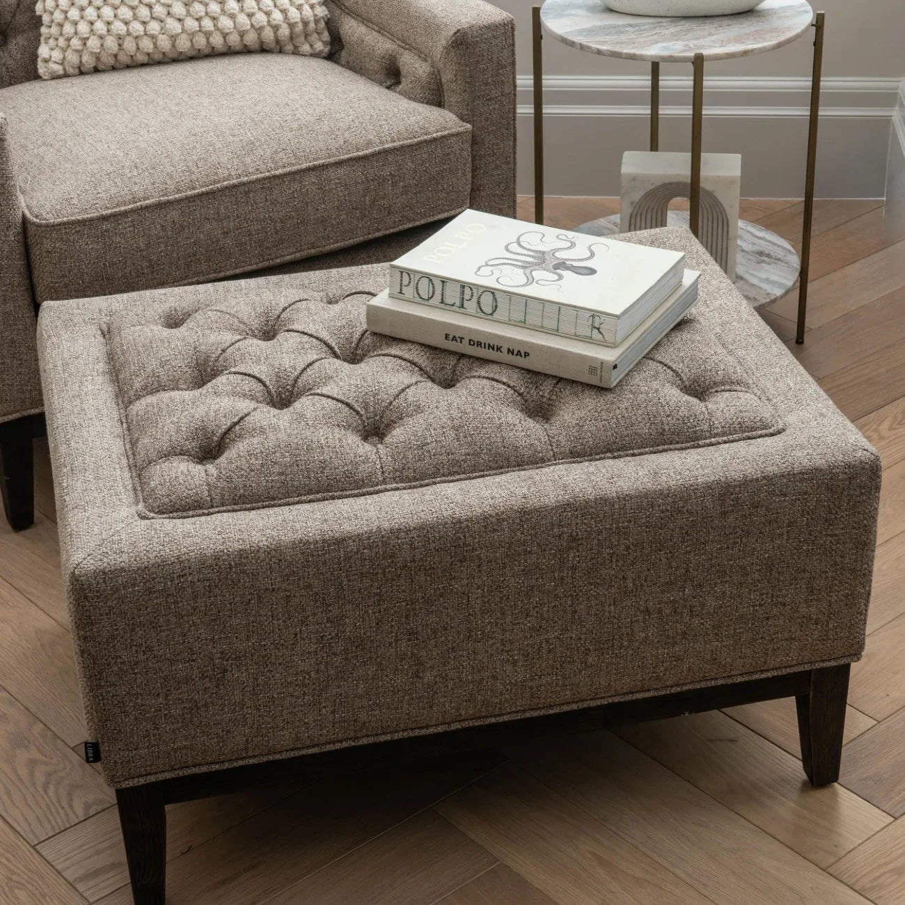 Dark taupe stool with buttoned top in cozy living room setting.