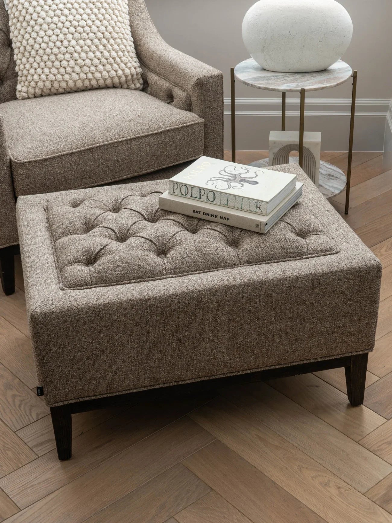 Dark taupe stool with buttoned top in cozy living room setting.