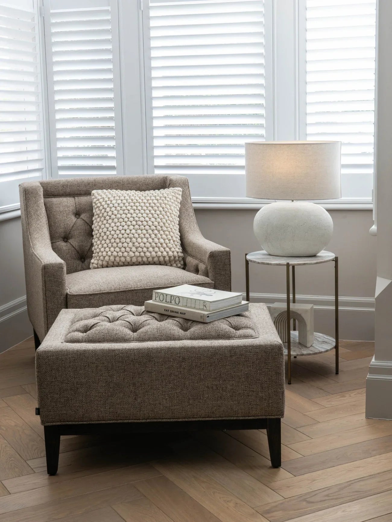 Dark taupe buttoned stool in cozy living room with armchair and lamp.