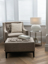 Dark taupe buttoned stool in cozy living room with armchair and lamp.