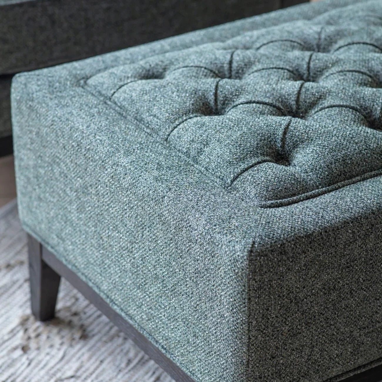Forest green stool with buttoned upholstery and dark wooden legs.