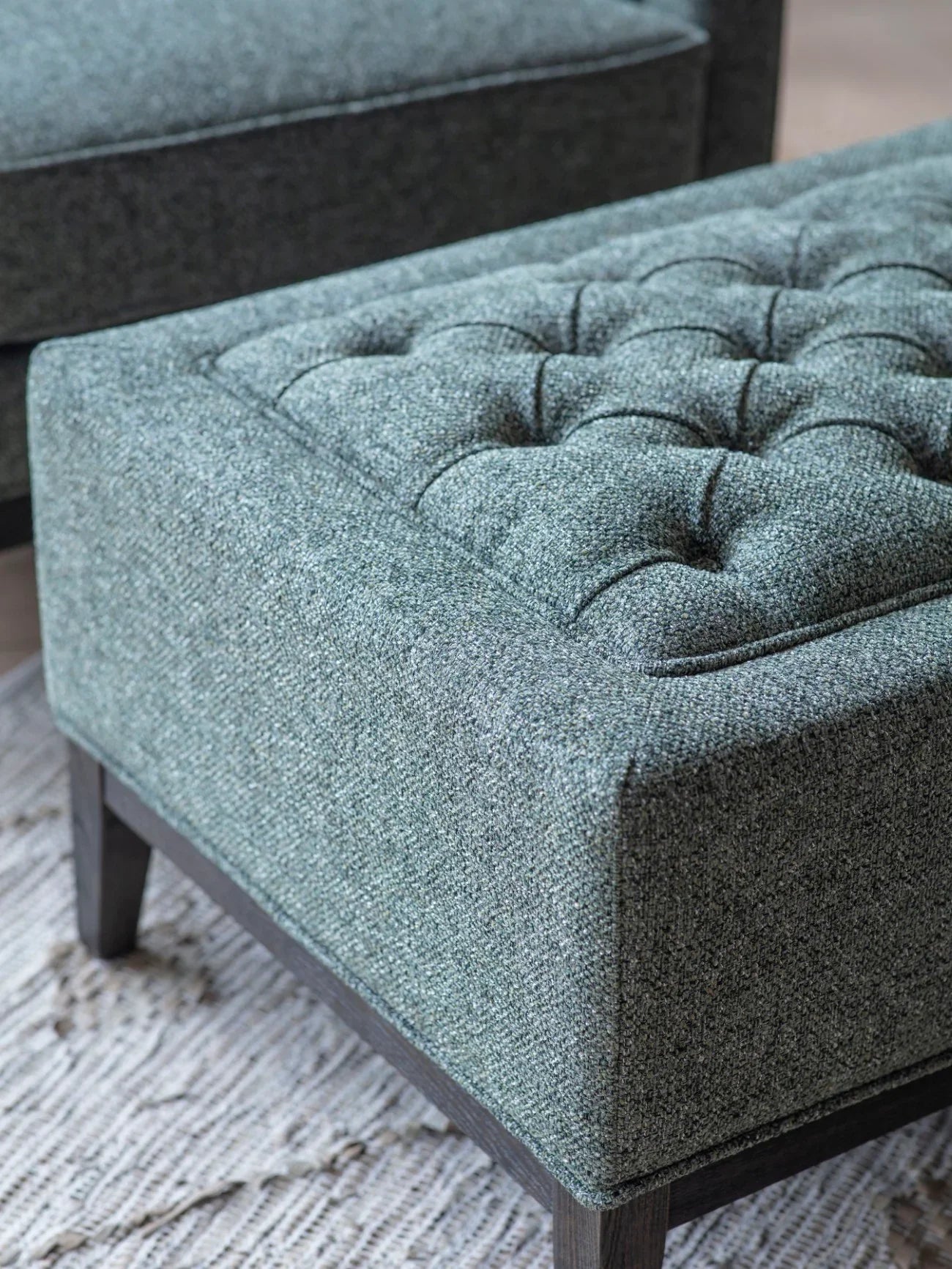 Forest green stool with buttoned upholstery and dark wooden legs.