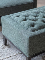Forest green stool with buttoned upholstery and dark wooden legs.