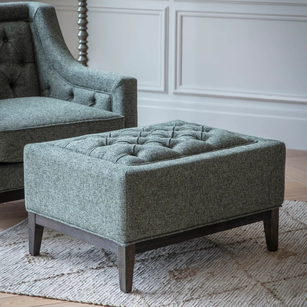 Forest green stool with buttoned top on a patterned rug.
