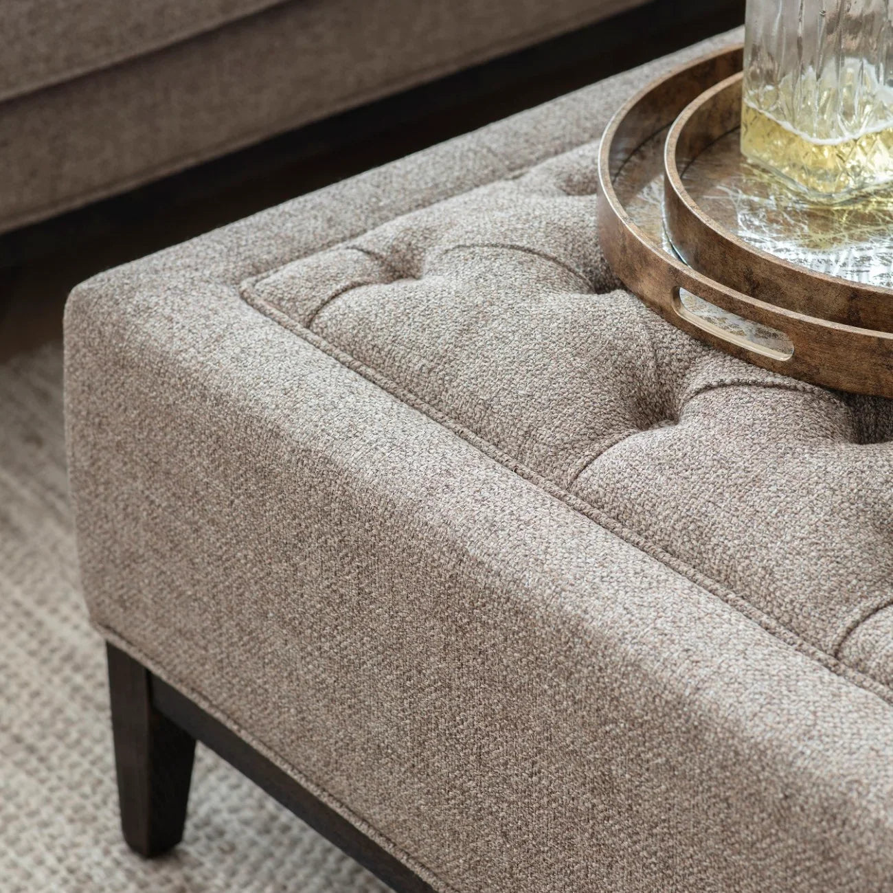 Dark taupe ottoman with buttoned texture and wooden tray on top.