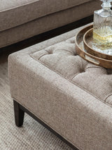 Dark taupe ottoman with buttoned texture and wooden tray on top.