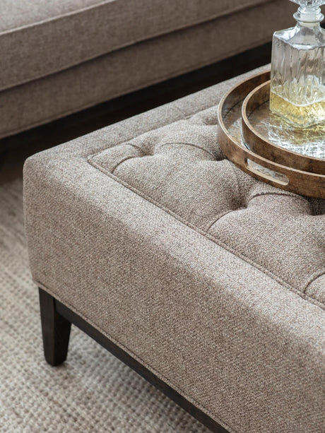Dark taupe ottoman with buttoned texture and wooden tray on top.