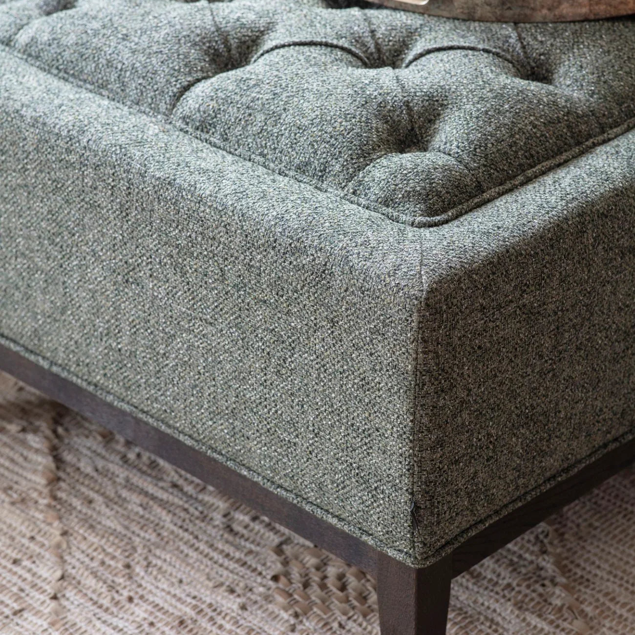 Forest green ottoman with buttoned texture and dark wooden legs.