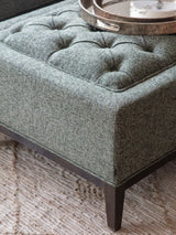 Forest green ottoman with buttoned texture and dark wooden legs.