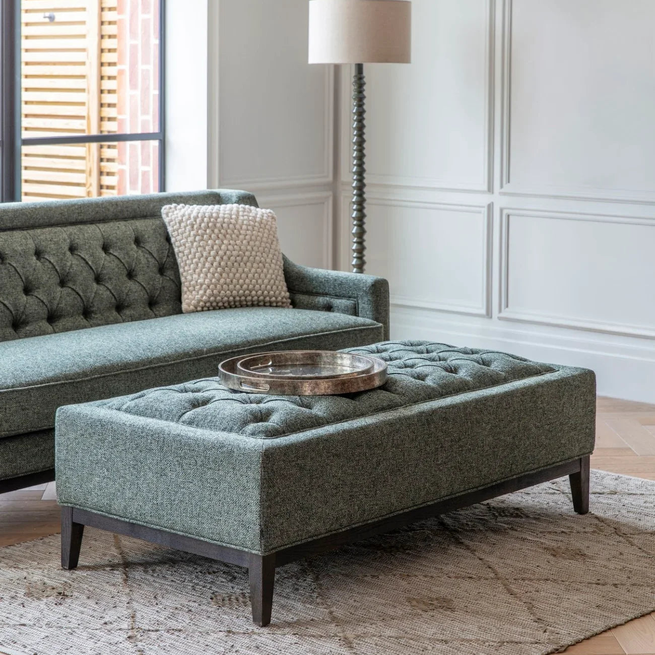 Forest green ottoman in elegant living room with sofa and floor lamp.