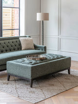 Forest green ottoman in elegant living room with sofa and floor lamp.