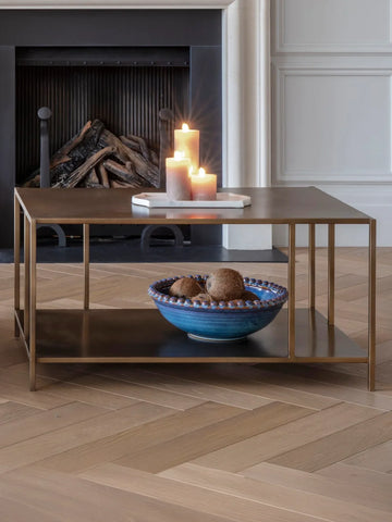 Brushed champagne coffee table with candles and a blue bowl in a cozy living room.