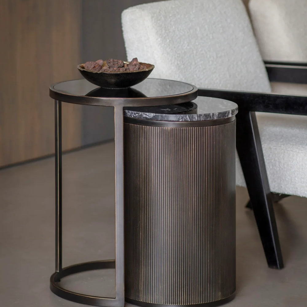 Black nesting tables with ribbed texture beside cream armchairs.