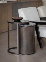 Black nesting tables with ribbed texture beside cream armchairs.