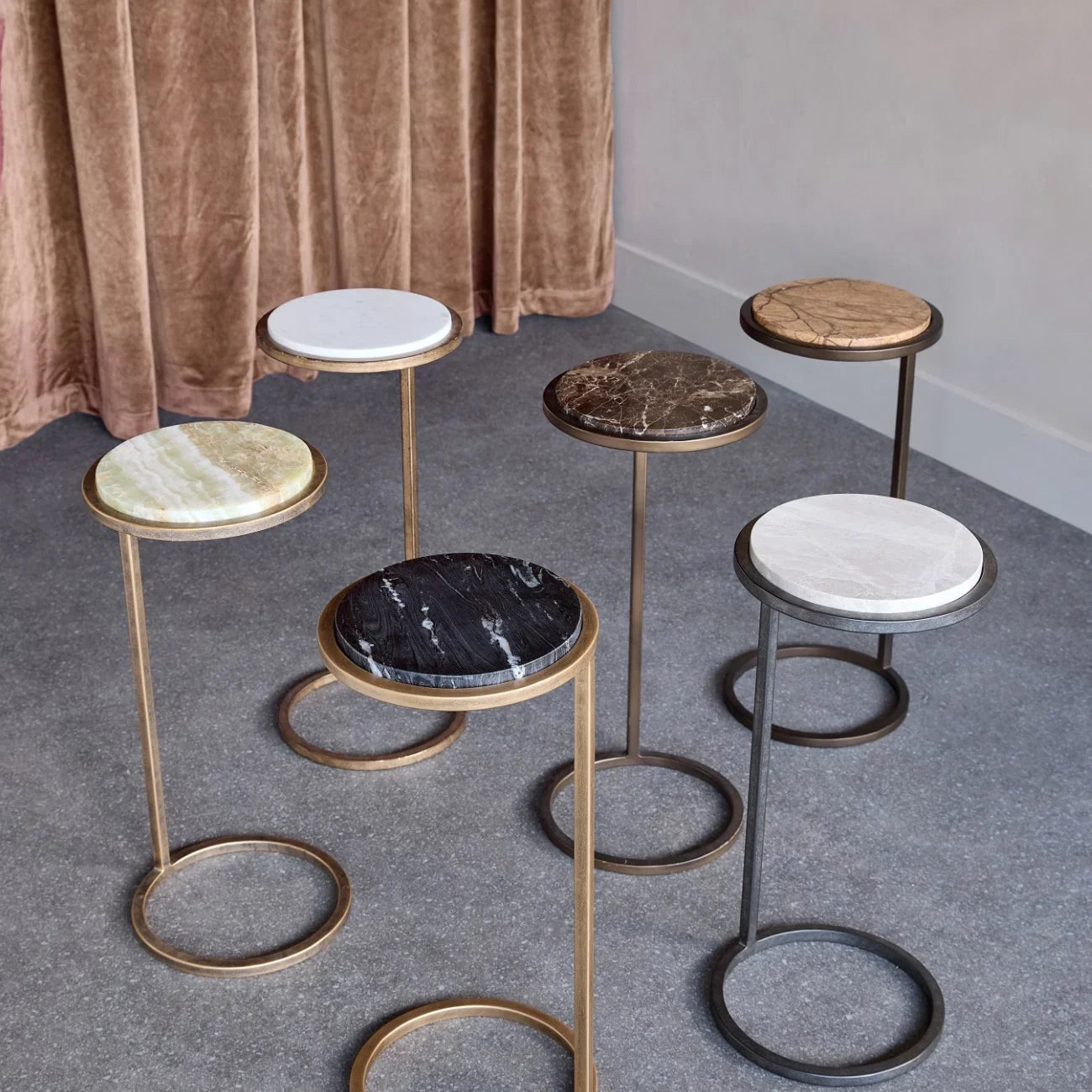 Assorted marble accent tables with metal bases on a textured floor.