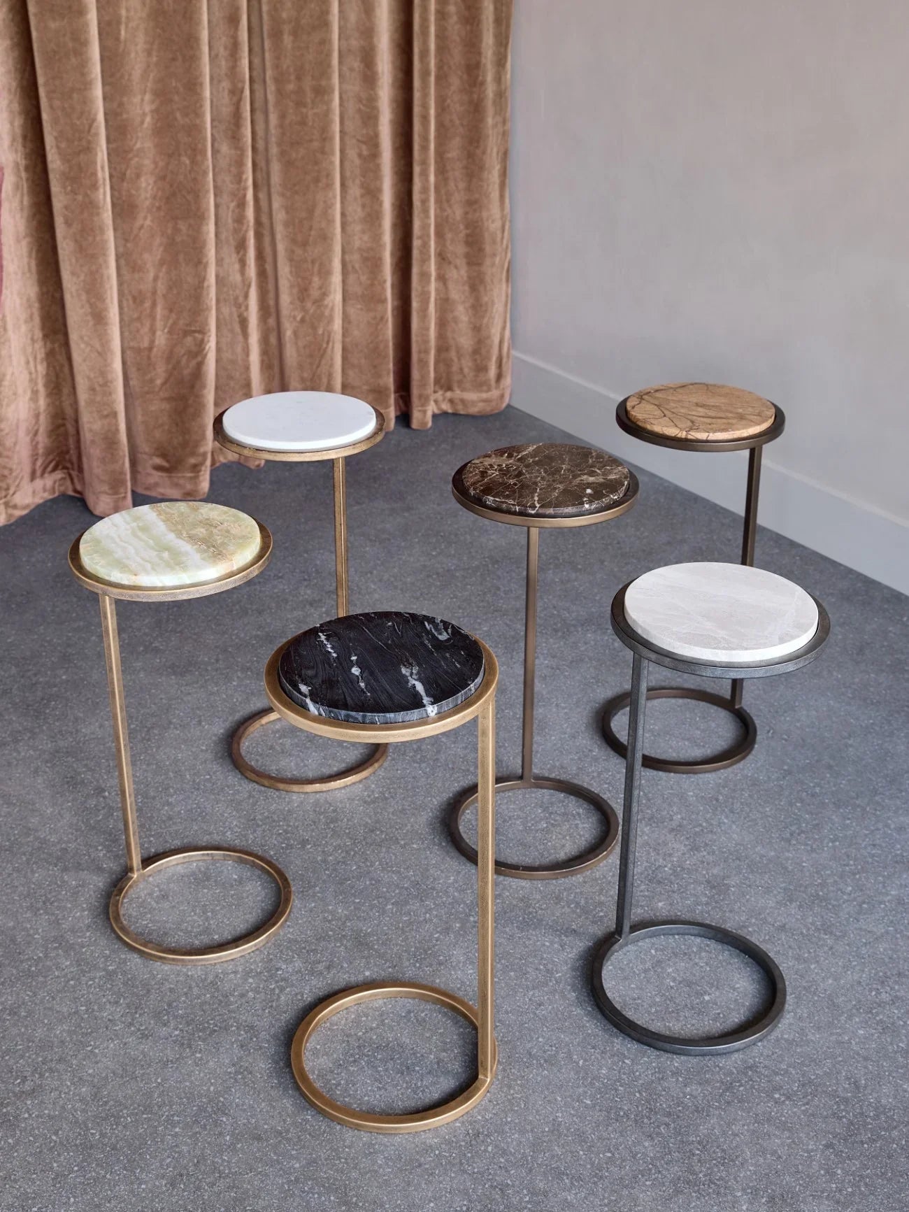 Assorted round side tables with marble tops on a textured floor.