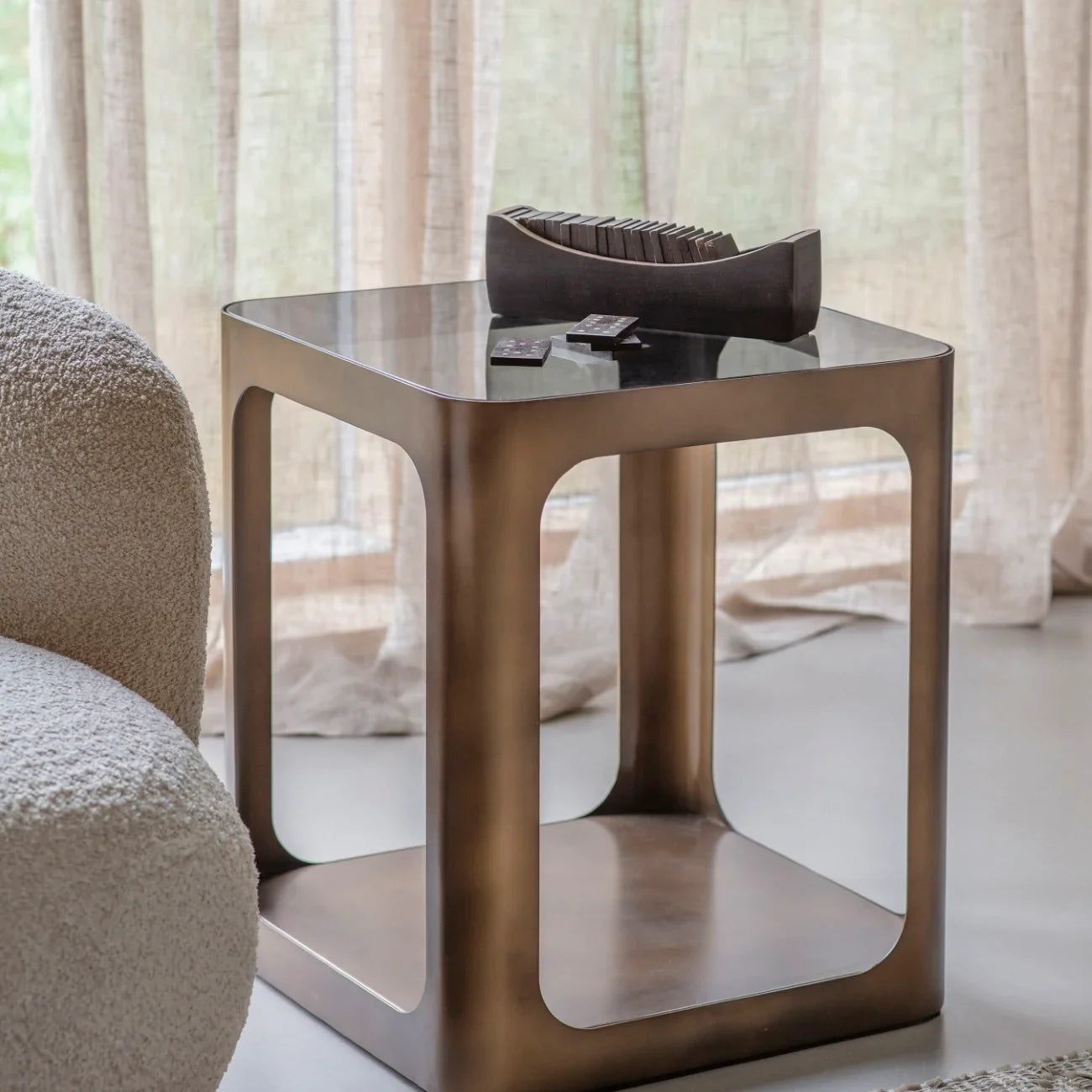 Bronze metal and glass side table beside a textured armchair in a cozy room.