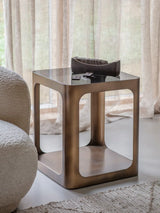 Bronze metal and glass side table beside a textured armchair in a cozy room.