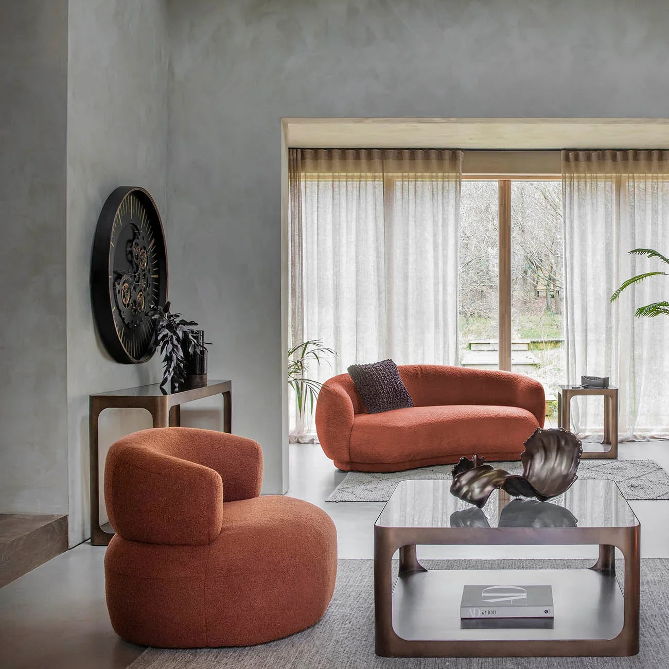 Glass and metal coffee table in a modern living room with rust-colored seating.