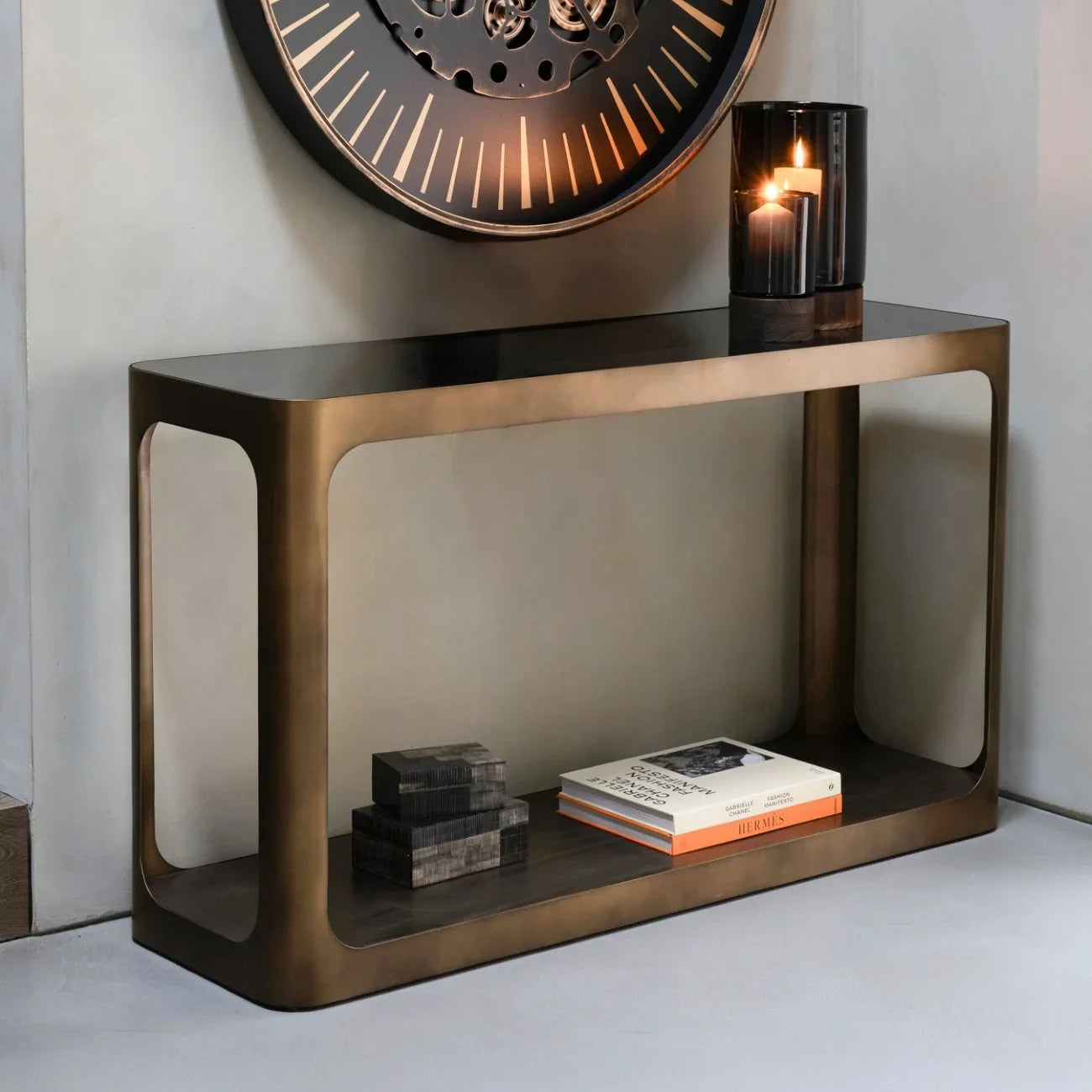 Bronze console table with books and candle, styled under a large wall clock.