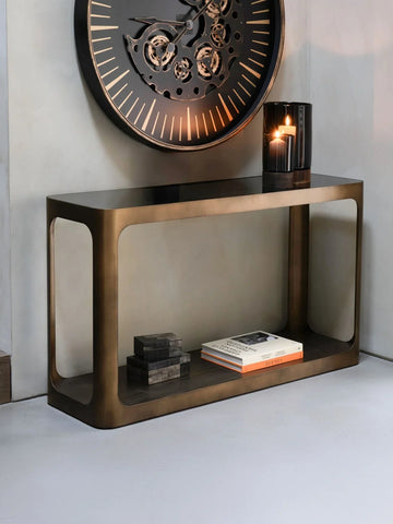 Bronze console table with books and candle, styled under a large wall clock.