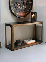 Bronze console table with books and candle, styled under a large wall clock.