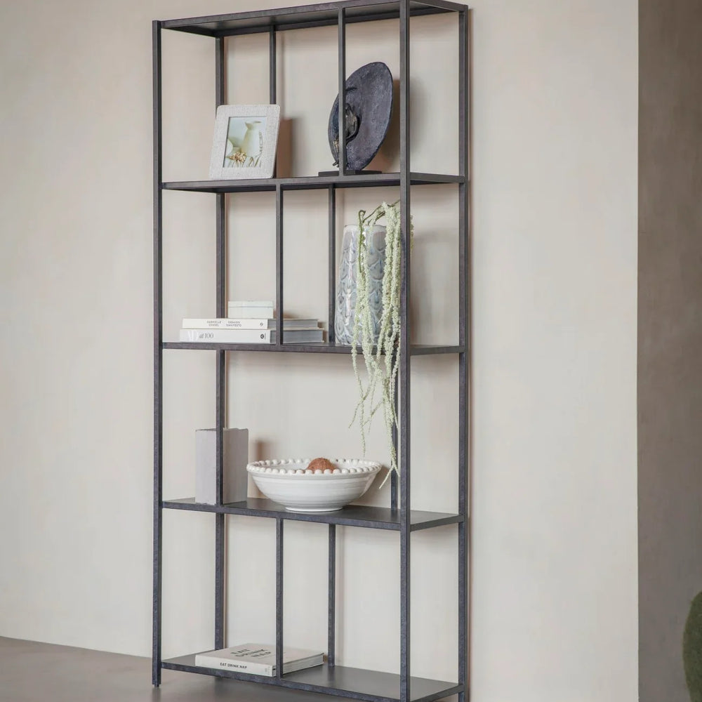 Mottled black metal shelving unit with decor items against a beige wall.